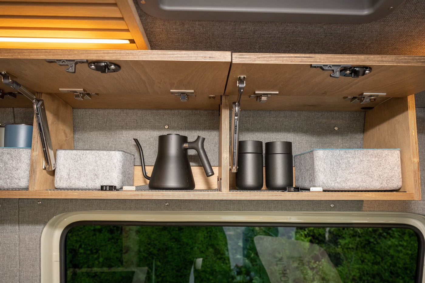 RV rental interior storage: Open cabinet with sleek black kettle, travel mugs, and felt organizers. Practical amenities for trips. — photo 14