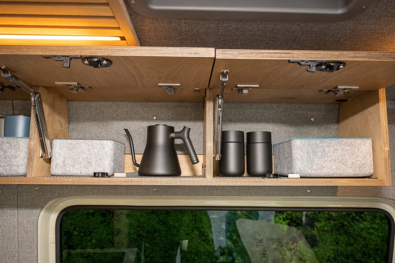 RV rental interior storage: Open cabinet with sleek black kettle, travel mugs, and felt organizers. Practical amenities for trips. — photo 14