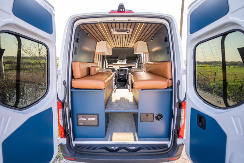 Inside a stylish RV rental: tan benches, wood ceiling, and back doors open to a tranquil green field and blue sky. — photo 15
