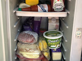 Compact fridge in an RV rental, packed with condiments, salad, protein drink, deli meat, cheese, and dip for road trip meals.