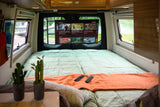 Relax in this rv rental's cozy bedroom featuring a TV with YouTube, a comfortable bed, remotes, and serene lake views outside.