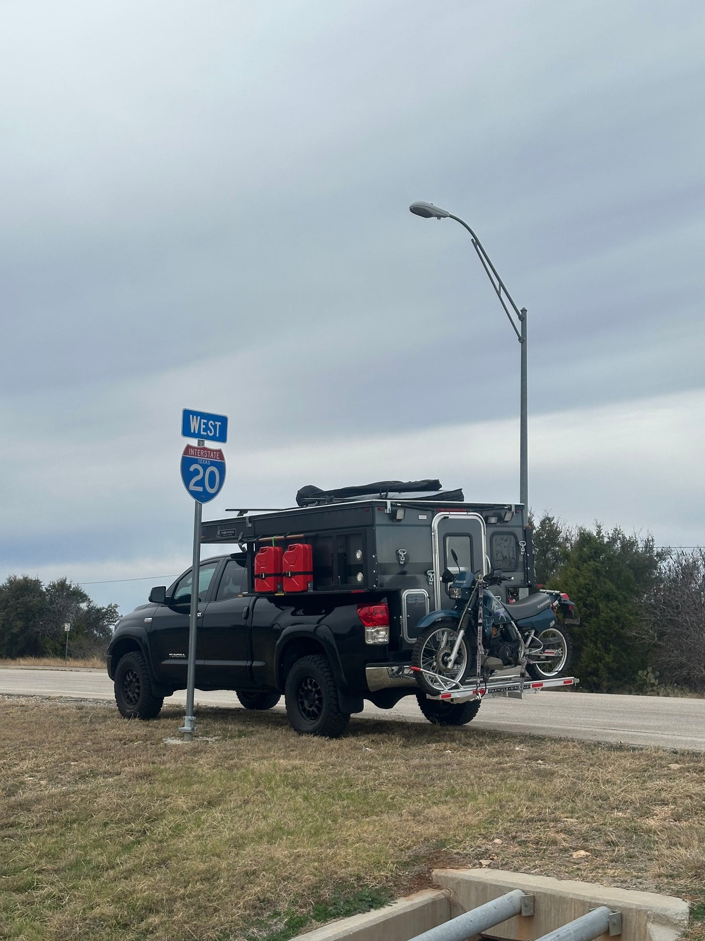  at a medical clinic.|An overland truck camper on a dirt mountain road with a person walking. Perfect for rugged travel. Consider an RV rental adventure!|Mud-splashed black Toyota Tundra overlanding truck with rooftop tent and gear — photo 5