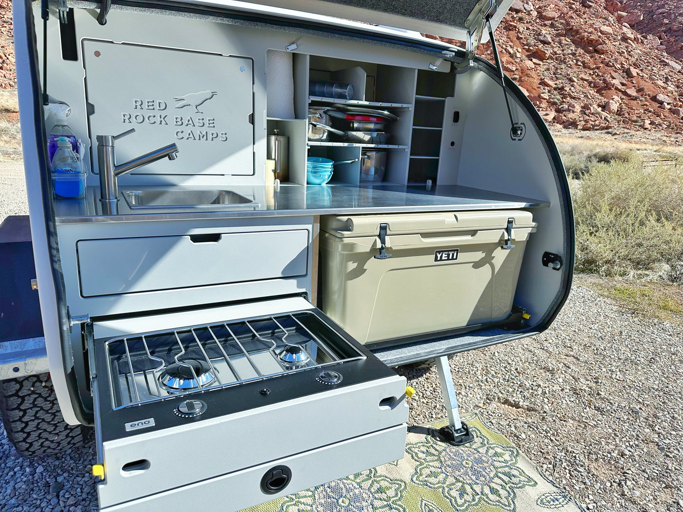 An RV rental showing a fully equipped pull-out outdoor kitchen with a sink, stove, and cooler, ideal for camping. — photo 10