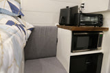 Compact RV rental interior featuring a kitchen setup with an air fryer, toaster oven, microwave, fridge, seating, and bed.