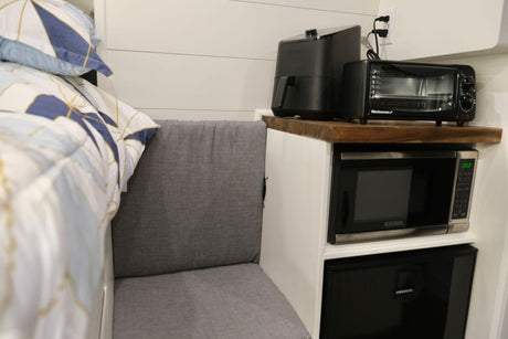 Compact RV rental interior featuring a kitchen setup with an air fryer, toaster oven, microwave, fridge, seating, and bed.