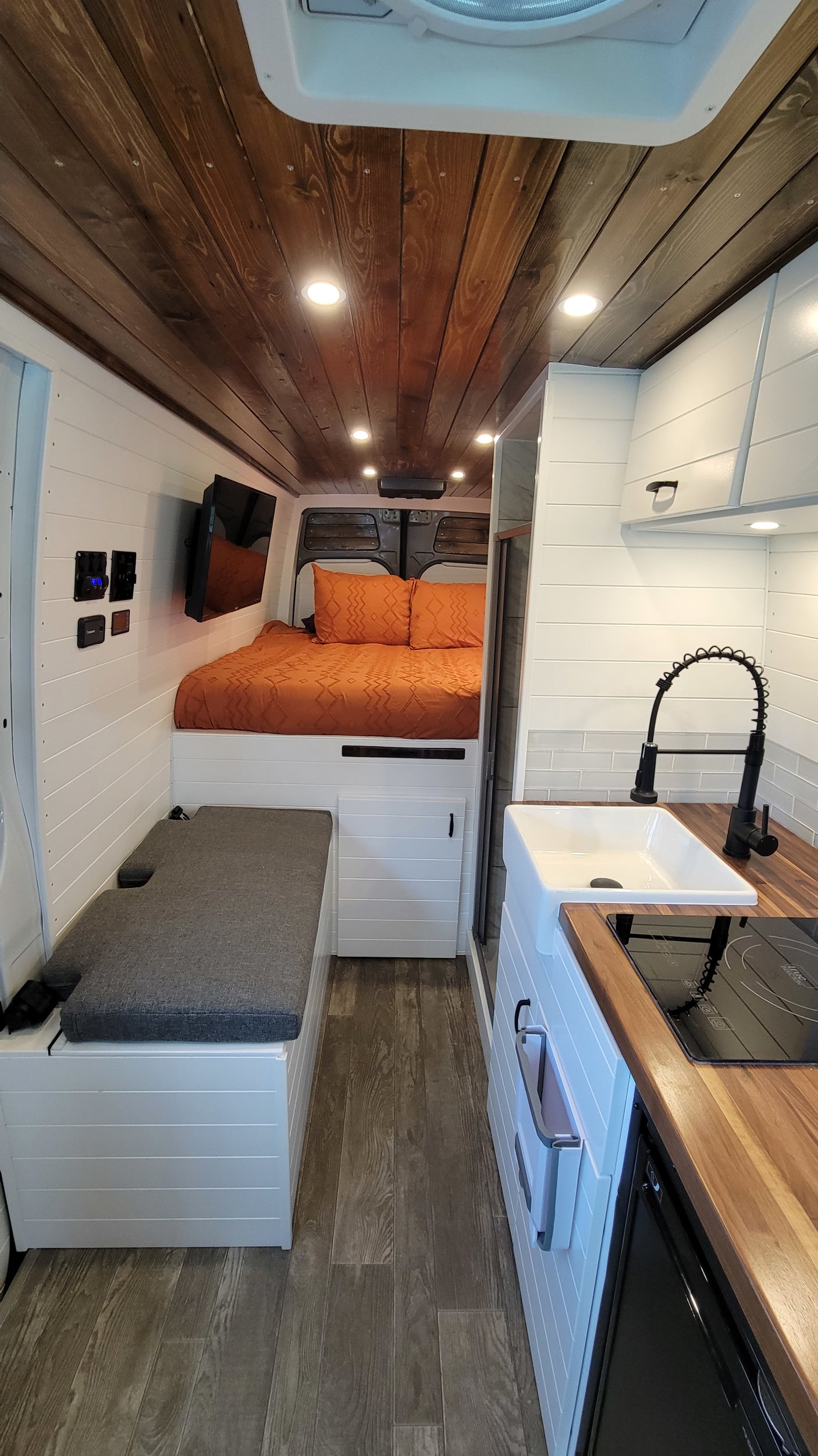 Step inside this cozy RV rental camper van! Modern interior with wood ceiling, white walls, bed, kitchen, and versatile bench seating.
