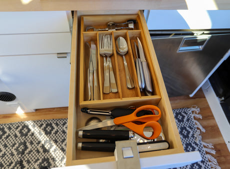 Inside an RV rental, a well-organized kitchen drawer displays silverware, knives, peeler, and scissors in a wooden tray.
