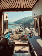 Inside an RV rental, a stunning view of a coastal campground, complete with beach, pier, and lush hills.