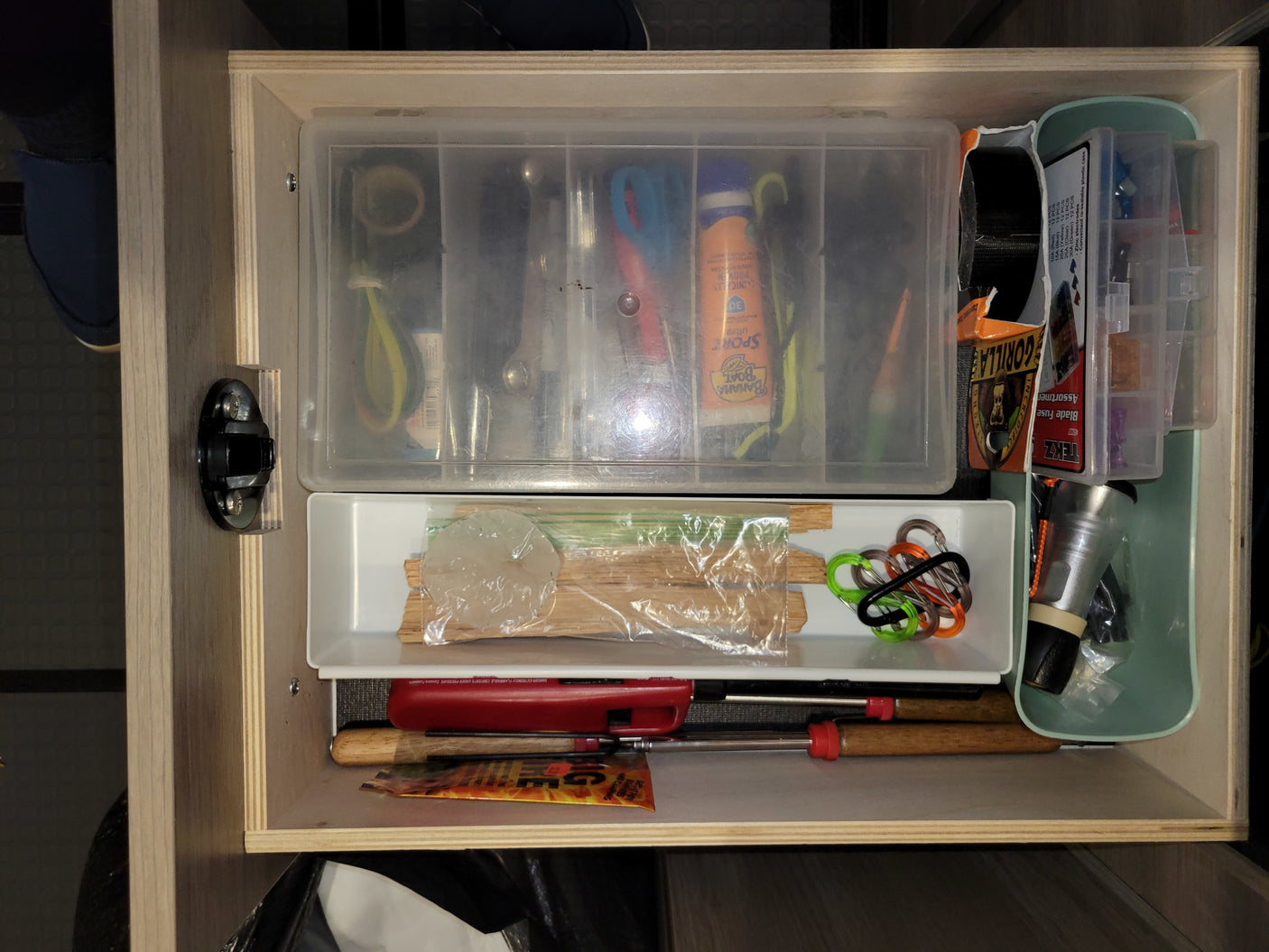 RV rental utility drawer with sunscreen, fuse assortment, carabiners, and fire starting tools, neatly organized.