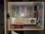 RV rental utility drawer with sunscreen, fuse assortment, carabiners, and fire starting tools, neatly organized.