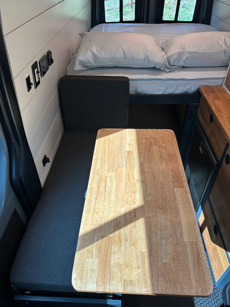 Bright RV rental interior showing a versatile dinette table, bench seat, and elevated bed area.