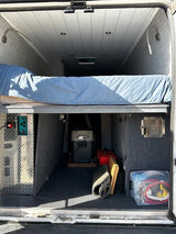 Inside an RV rental: organized camper van interior with raised bed, ample storage, electrical setup, and portable fridge.