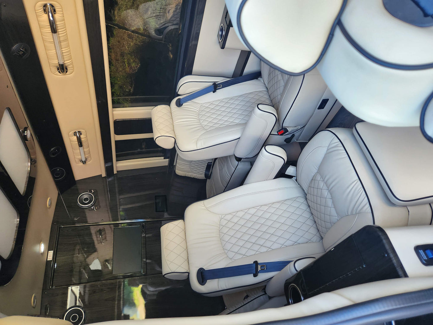 Luxury RV rental interior: cream leather captain's chairs with blue seatbelts, wood-grain floor, and spacious comfort.