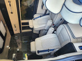 Luxury RV rental interior: cream leather captain's chairs with blue seatbelts, wood-grain floor, and spacious comfort.
