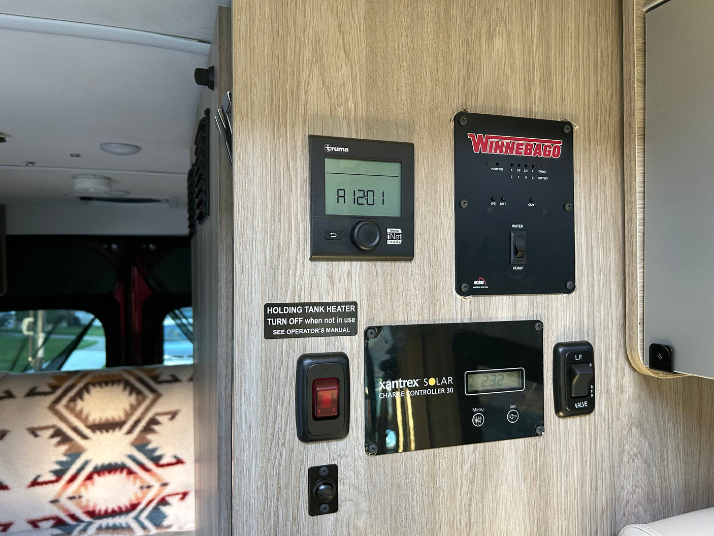 RV rental interior control panel featuring Truma heater, Winnebago monitors, Xantrex solar charger, and tank heater controls.