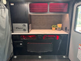 This RV rental showcases a compact interior with a "Flyer" cooler, modern countertop, and red-lit storage ideal for travel.