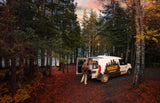 Experience autumn camping with this Voyager campervan RV rental by a lake, featuring a campfire and a person setting up in the forest.