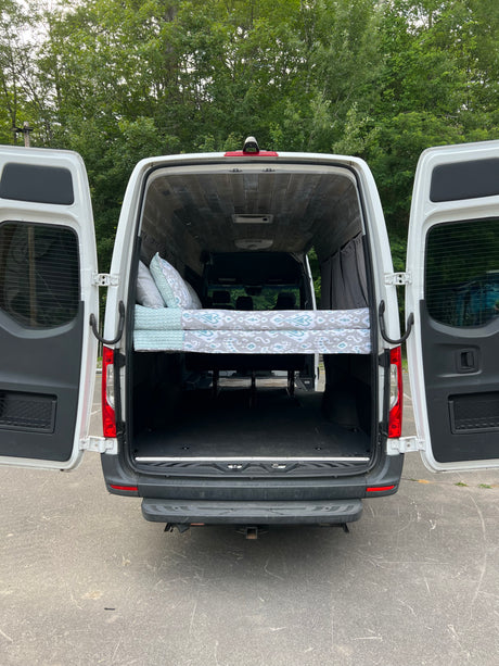 Rear view of a spacious camper van conversion. Elevated bed and ample storage visible. Ideal for rv rental.