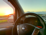 Golden sunset view from a Nissan car. Dashboard and side mirror show road & mountains, evoking a scenic RV rental road trip.
