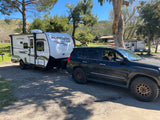 RV rental ready for a camping trip! White Surfside travel trailer hitched to a dark SUV with a child smiling from the window.