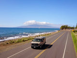 Scenic Hawaii coastal drive with an RV rental van and ocean views, sailboat in the distance.