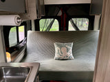 Inside a comfortable rv rental: Kitchenette, striped seating/bed, and a view of the outdoors with trees and people.