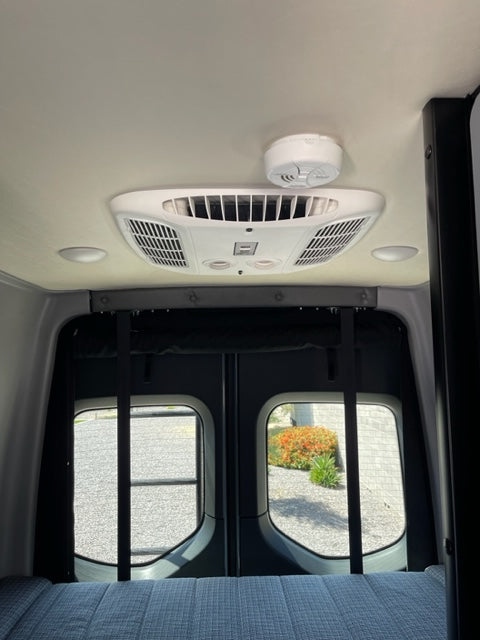 RV rental interior: Features a white ceiling-mounted AC unit, a smoke detector, and two large side windows.