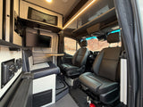 Inside a modern RV rental: a comfortable dinette, entertainment system, and spacious cockpit, framed by scenic desert views.