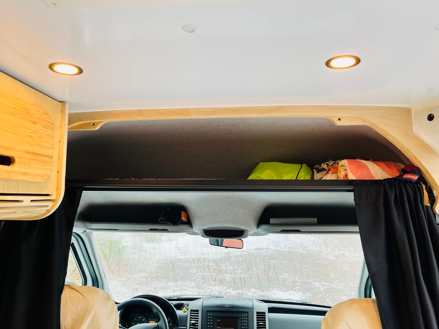 Cozy RV rental interior with overhead storage, warm lighting, and a view of a snowy landscape through the windshield.