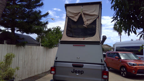 This grey Jeep Gladiator pickup with a tan pop-up camper, an excellent RV rental option for outdoor adventures and overlanding.