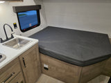 RV rental interior: a compact kitchen with a stainless steel sink and black faucet on the left, beside a dark gray bed.
