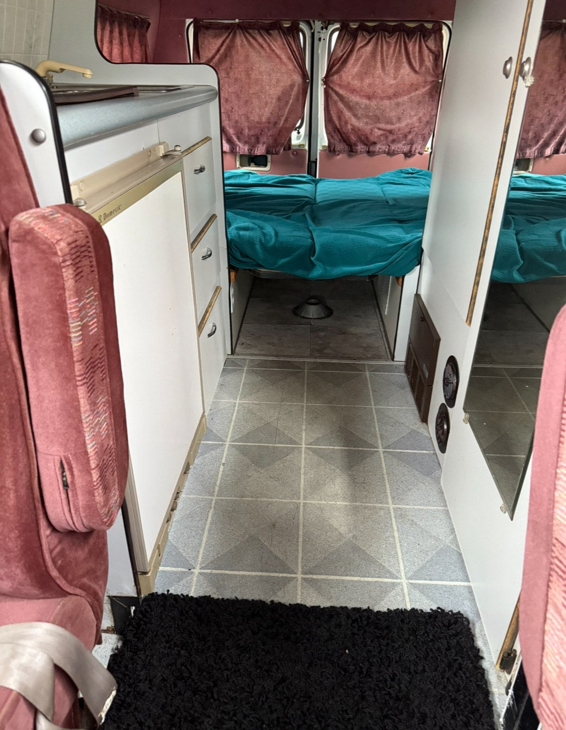  showing a bed with a blue pillow and light knitted blanket under a low ceiling.|RV rental interior: A beige pillow rests on a teal blanket-covered bed — photo 10