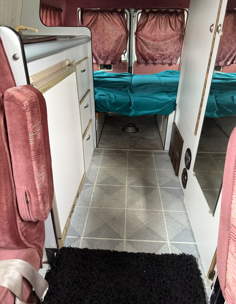  showing a bed with a blue pillow and light knitted blanket under a low ceiling.|RV rental interior: A beige pillow rests on a teal blanket-covered bed — photo 10