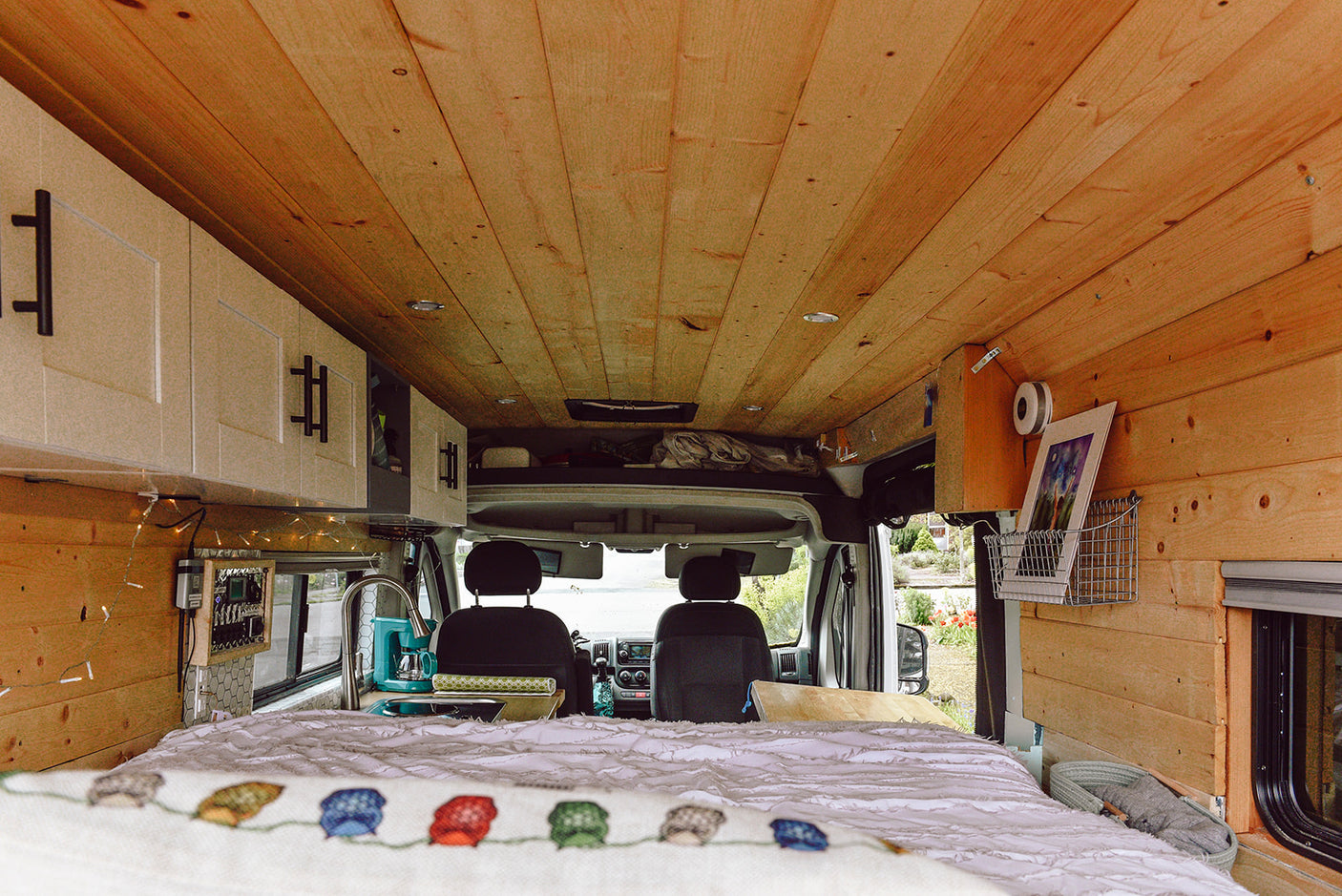 Cozy RV rental interior with wood-paneled walls/ceiling, bed, white cabinets, and front seats visible, perfect for van life.