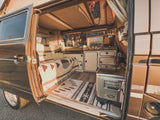 Interior of a classic Westfalia camper with kitchen, bed, and Coleman fridge, ideal for an RV rental getaway.