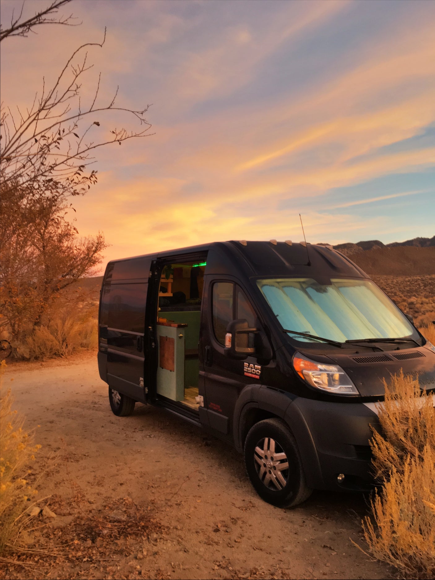 Black rv rental camper van parked on dirt road at desert sunset. Experience cozy van life adventures.