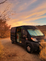 Black rv rental camper van parked on dirt road at desert sunset. Experience cozy van life adventures.