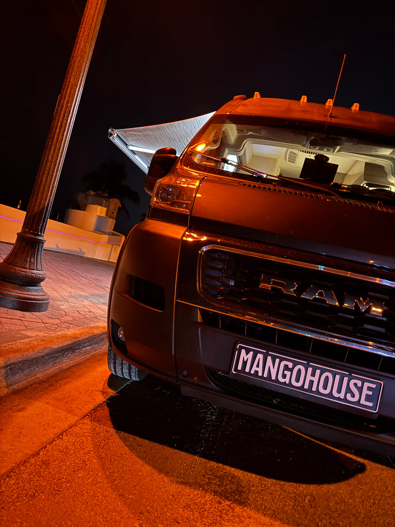 A sleek, dark MANGOHOUSE rv rental camper van with an extended awning, parked under warm, glowing lights at night. — photo 20