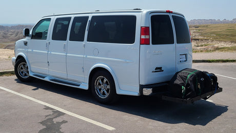 White RV rental conversion van with rear cargo carrier, parked at a scenic Badlands overlook.
