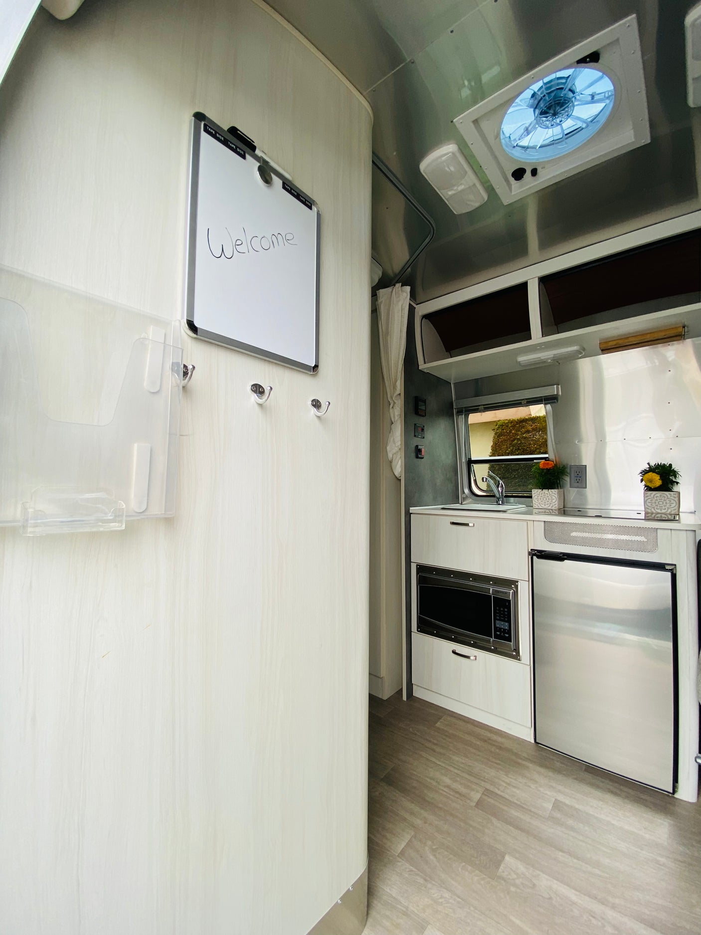 Welcome inside this RV rental, featuring a modern kitchen with microwave, fridge, and a handy welcome board.