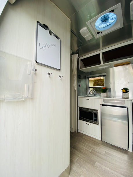 Welcome inside this RV rental, featuring a modern kitchen with microwave, fridge, and a handy welcome board.