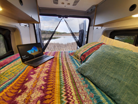 Cozy RV rental interior with bed, laptop, and scenic lake view. Perfect for remote work and travel.