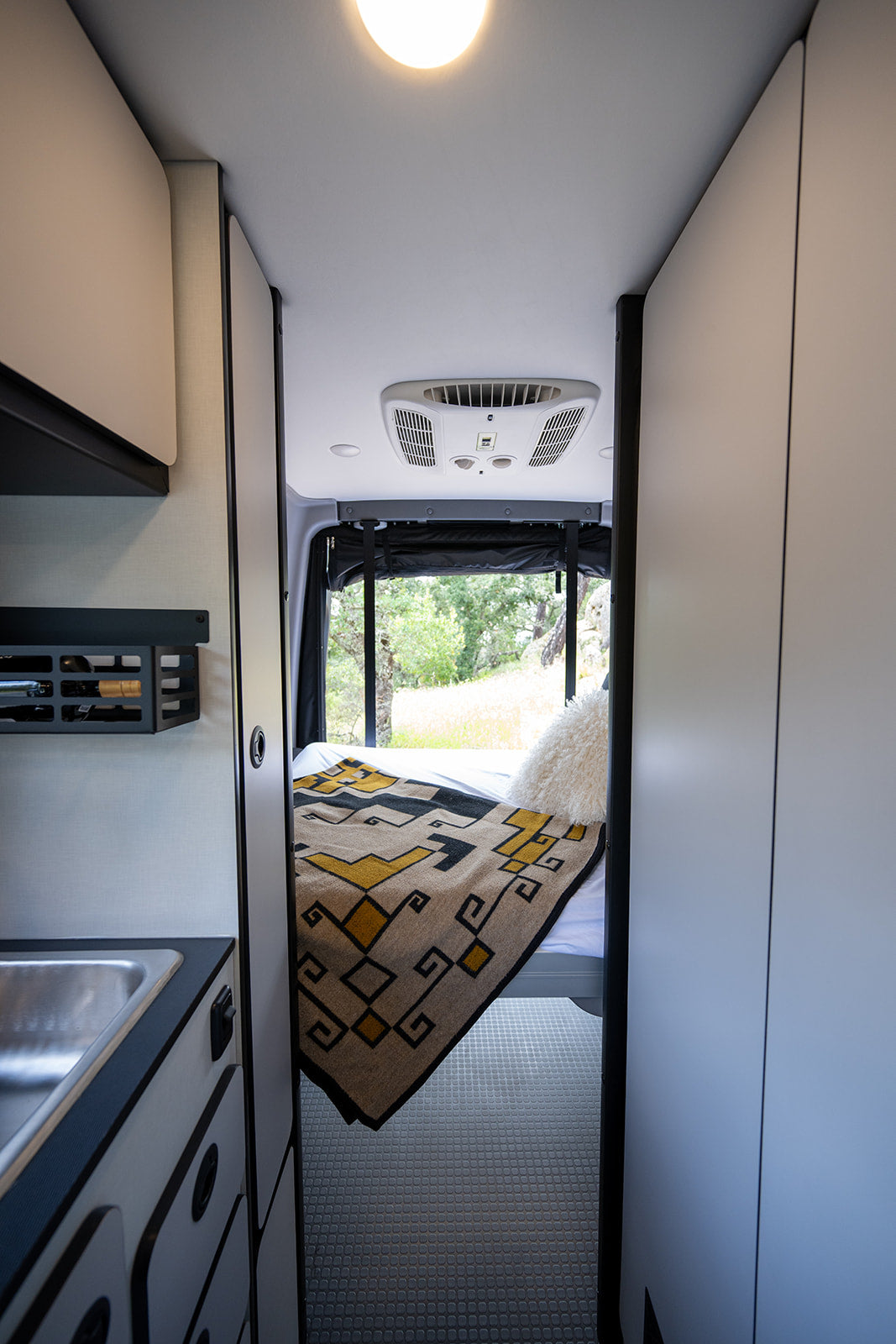 Explore this RV rental's modern interior: cozy bed, sink area, AC unit, and natural views outside. Ideal for adventures.