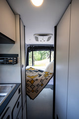 Explore this RV rental's modern interior: cozy bed, sink area, AC unit, and natural views outside. Ideal for adventures.