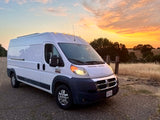 This white Ram ProMaster camper van RV rental, parked at sunset by rolling hills, is ready for your next outdoor adventure.