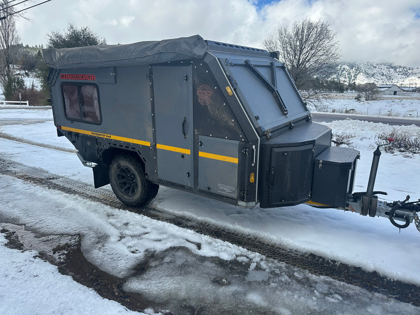 Conqueror 4x4 off-road camper trailer on a slushy, snowy road with mountains. Perfect for an adventurous rv rental!