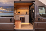 Modern RV rental camper van interior. See the custom kitchen, bed, and warm wood finishes, ready for adventure.