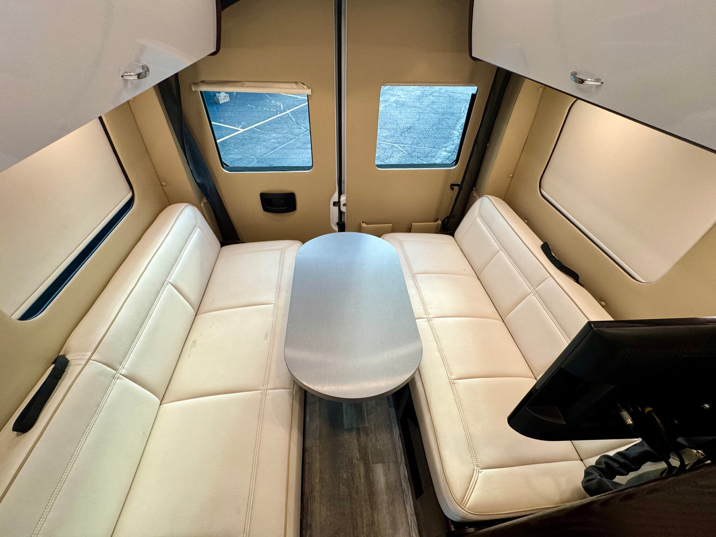 Bright rv rental camper van interior with cream lounge seating, a central silver table, and a TV for comfy travel.