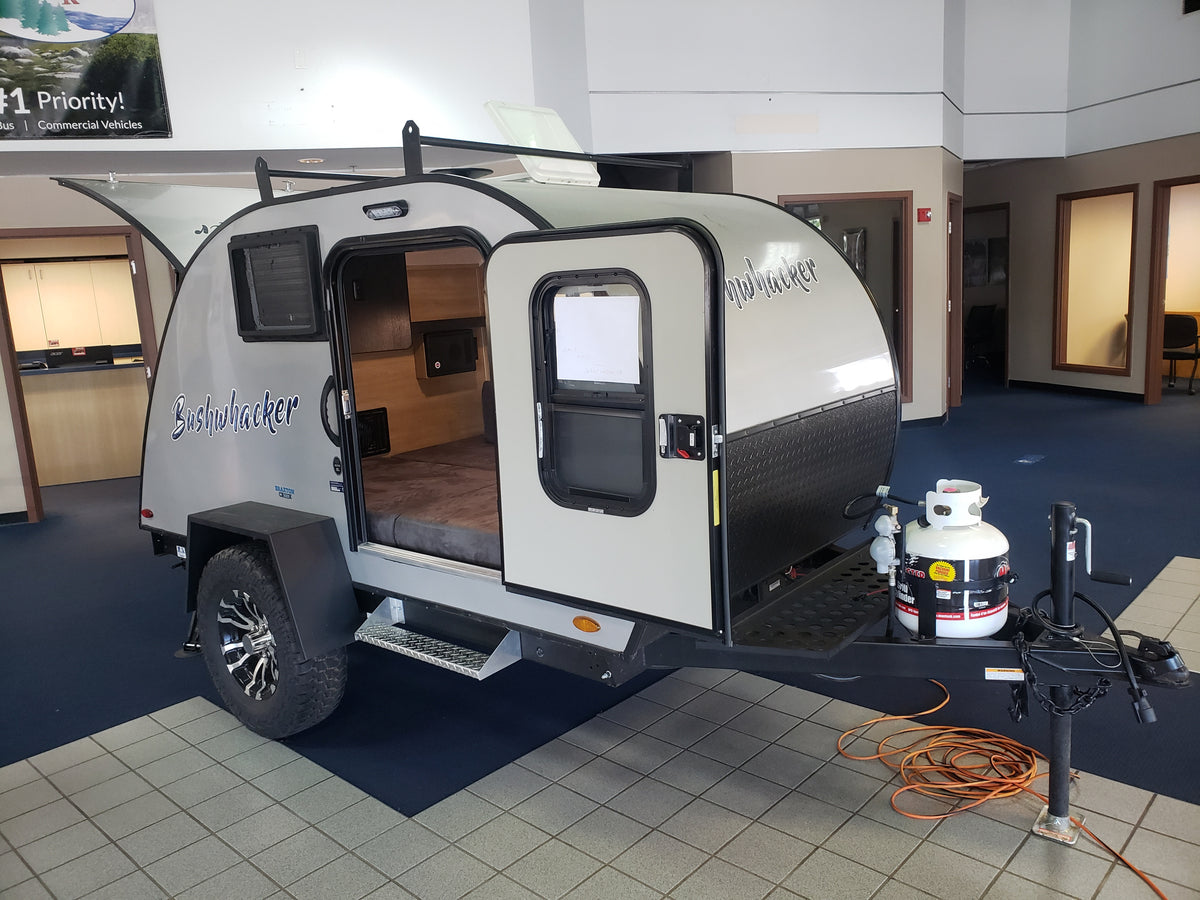 A Bushwhacker compact RV rental stands in a bright showroom, its open door inviting a look at the cozy bed. — photo 2