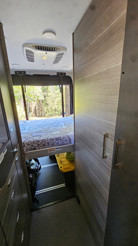 Inside an RV rental: rear bed, large window with forest view, AC, and under-bed storage. Ideal for travel.